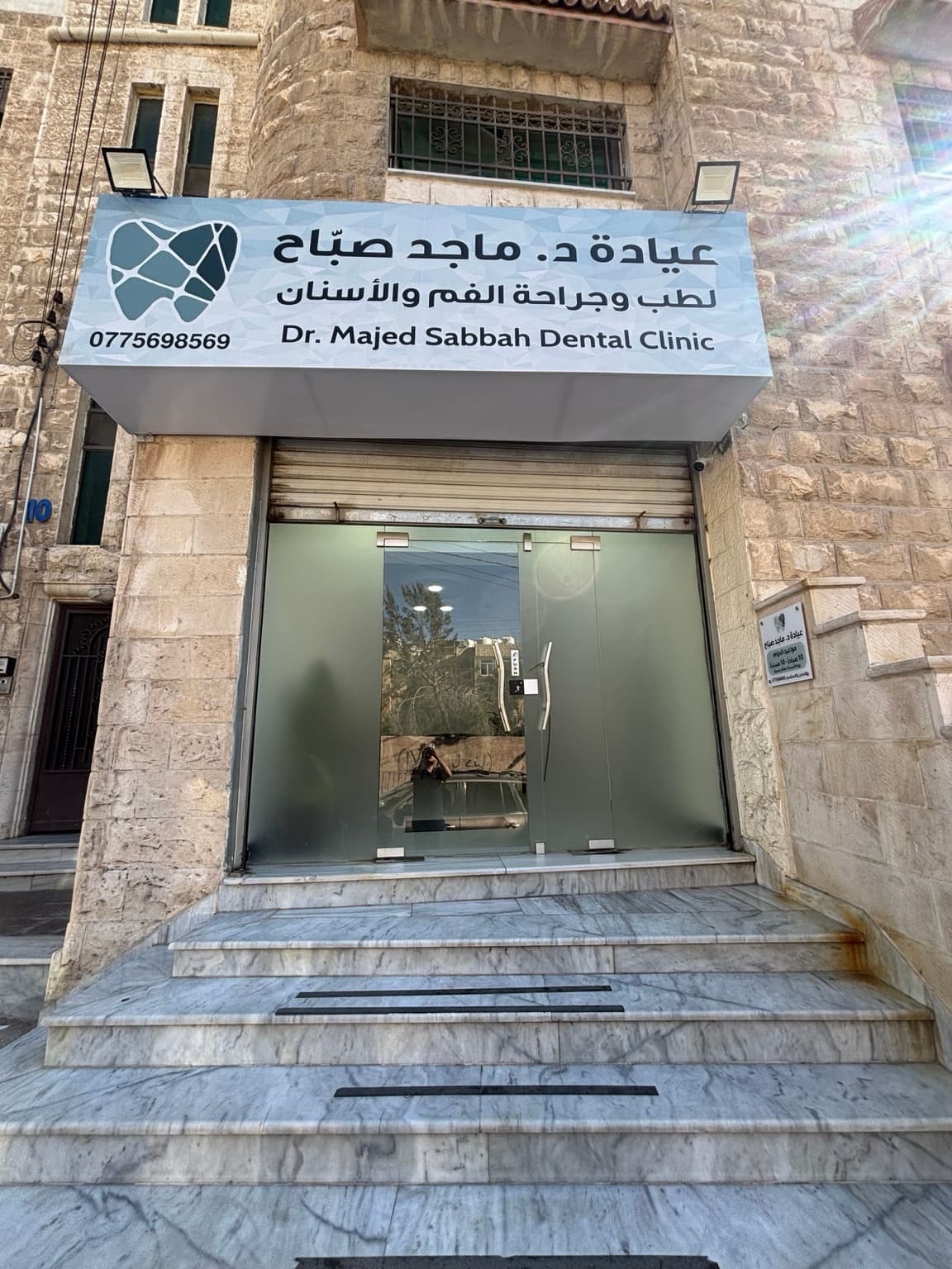 Entrance of Dr. Majed Sabbah Dental Clinic: clinic sign and logo above glass doors and marble steps Entrance of Dr. Majed Sabbah Dental Clinic: clinic sign and logo above glass doors and marble steps